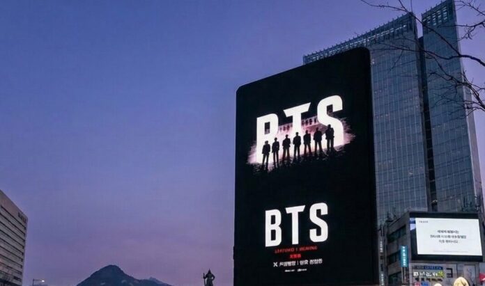 BTS billboard at Gwanghwamun Square with fans and police visible, Seoul, 2026